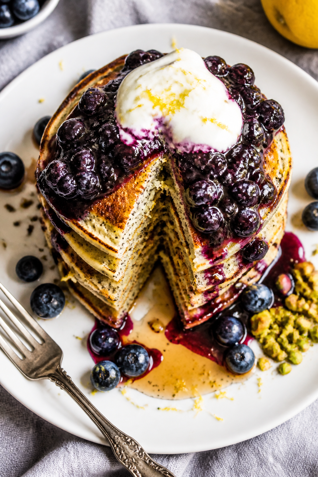 Final plated overhead: Tall stack of protein-packed lemon poppyseed pancakes on a matte white plate,